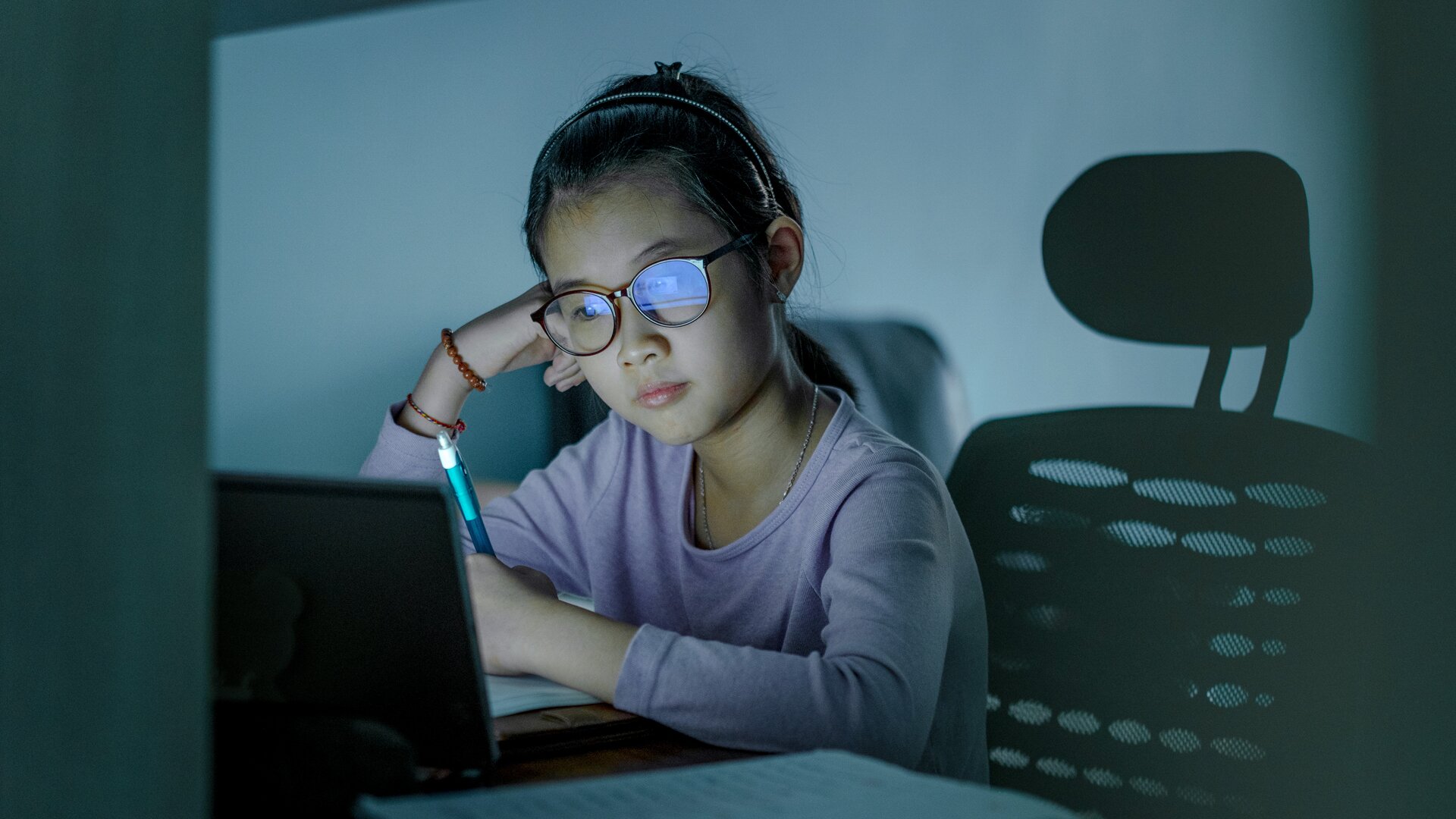 young girl with glasses sitting in front of a computer with a pen in her hand